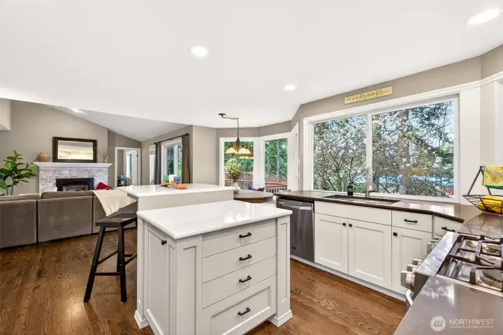 The updated kitchen is the heart of the home — featuring quartz countertops, a center island with bar seating, shaker cabinetry, stainless appliances, and a wraparound window overlooking the backyard and trees, all opening directly to the family room.