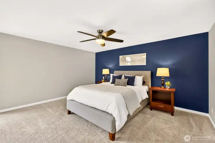 The generously sized primary bedroom offers a true retreat — with plush carpet, a ceiling fan, and a dramatic navy accent wall that adds a sense of depth and sophistication to this private upstairs sanctuary.