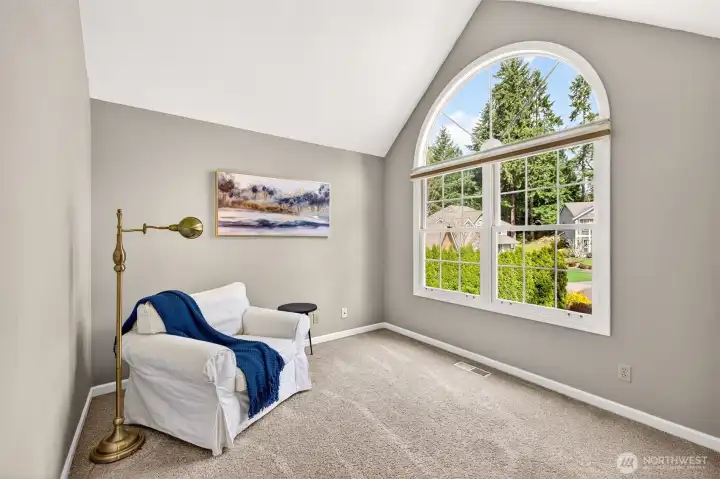 The primary suite's vaulted sitting area features a dramatic arched window framing a lush evergreen outlook — a serene, light-drenched space perfect for a morning reading nook or a quiet end-of-day escape.
