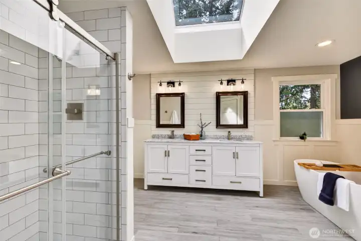 The updated primary bath is a true spa retreat — featuring a skylight that bathes the space in natural light, dual-sink vanity with marble countertops, shiplap accent wall, freestanding soaking tub, heated floors, and a walk-in tile shower.