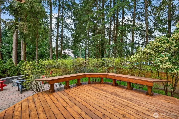 The expansive lower deck level features a custom built-in bench wrapping the perimeter — a generous, versatile outdoor space designed for effortless entertaining, summer gatherings, or simply enjoying the serene wooded backdrop.