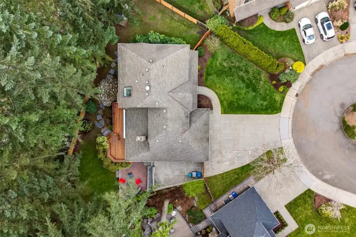 An aerial overview reveals the exceptional lot layout — showcasing the wide concrete driveway, lush front lawn, multi-level rear deck, patio, and the privacy-enhancing tree canopy that defines this English Hill setting.