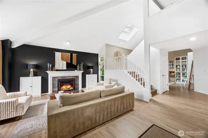 The formal living room features a dramatic floor-to-ceiling brick fireplace focal point, beautifully contrasted against clean white walls. Soaring architectural ceilings and massive windows flood the space with natural light.