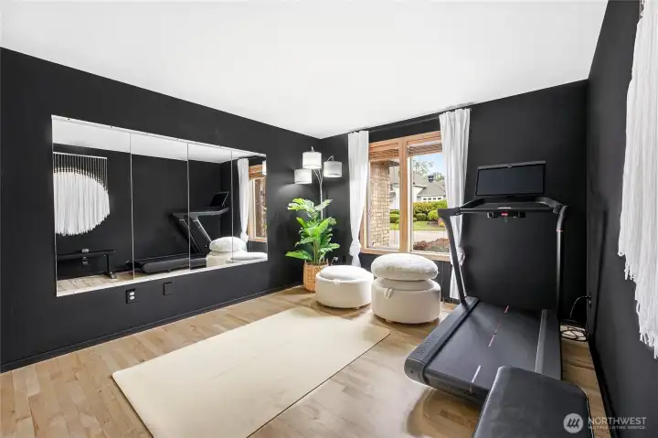 Multi-functional main-floor flex room or high-end home gym space, featuring a striking black accent wall, modern recessed LED lighting, and ample square footage to customize to your lifestyle. Easy den, office or 5th bedroom.