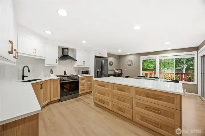 Gourmet chef’s dream kitchen completely modernized with premium light wood shaker cabinetry, an expansive central island with breakfast bar seating, and beautiful quartz countertops.