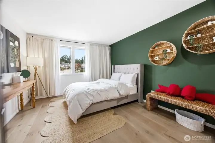 Second spacious upper-level bedroom featuring a striking deep-green accent wall, continuous premium wide-plank flooring, and an expansive window line that overlooks the peaceful neighborhood greenery.
