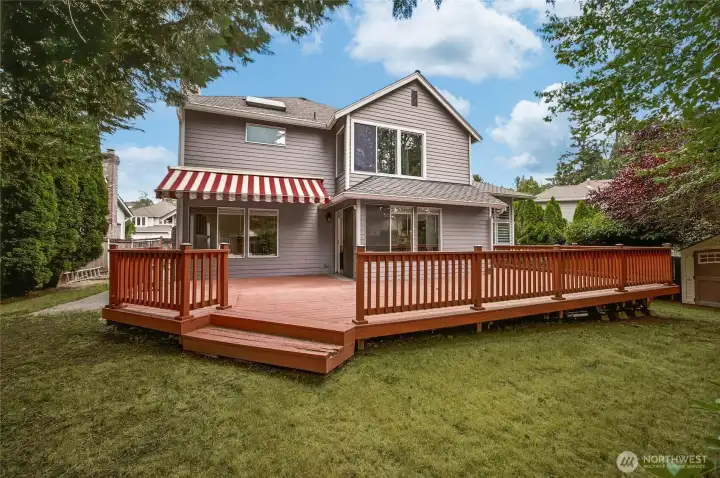 Rear exterior elevation showcasing the home's sturdy construction, expansive entertainment deck, and the massive, private backyard lot completely surrounded by mature PNW trees.