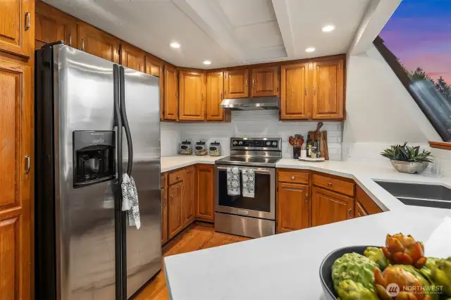 Brand new quartz countertops, stainless steel appliances, and a picture window view of the backyard and verdant evergreens from the from the kithcen sink to the backyard.