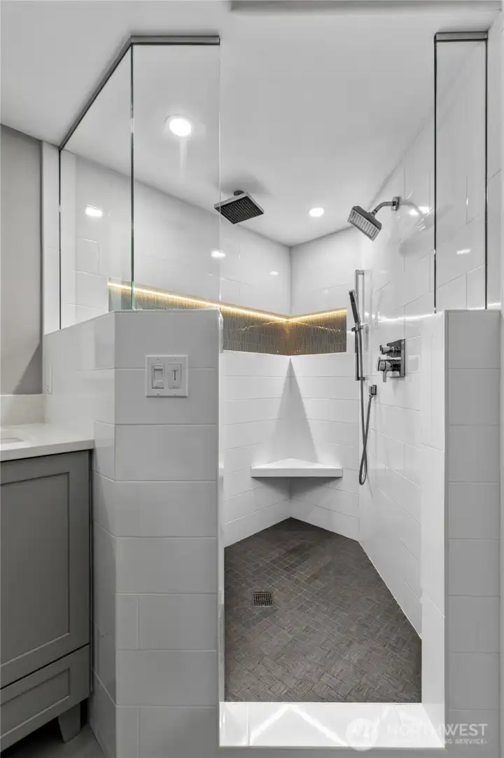 Large walk-in shower with two shower heads, built-in seating and inset, lighted shelf.