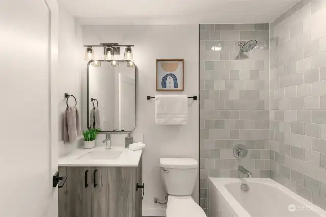 The secondary bedroom features own private bathroom with full tub, custom grey tile and vanity with under-sink storage!