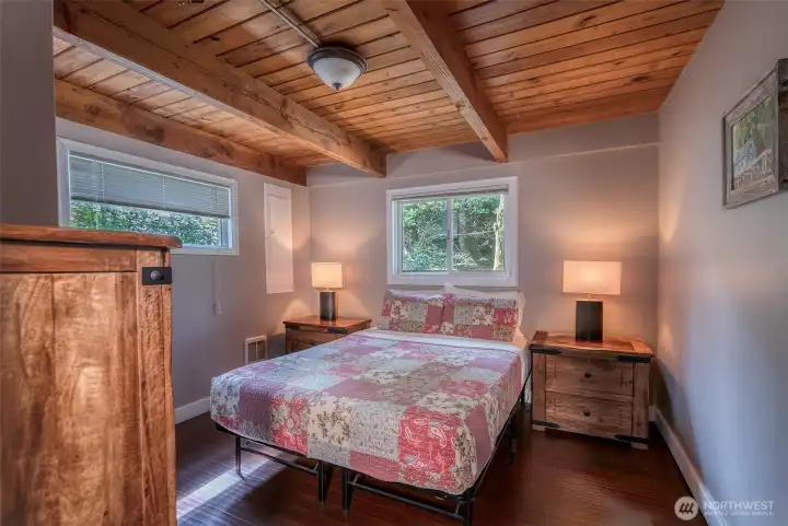 Warm & Inviting queen bedroom featuring rich, wood plank & beam ceilings, earthy finishes and soft natural light. Wood furnishings and clean lines create a cozy retreat feel w/a calming connection to nature views.