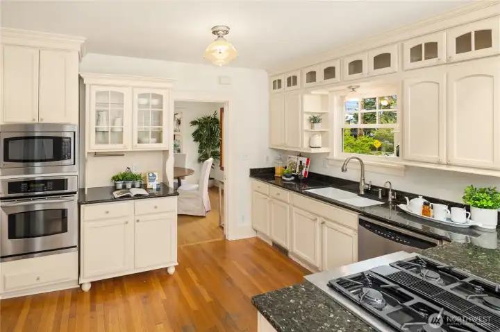 This view from the breakfast bar shows double-ovens, granite countertops, and a built-in hutch with display shelves.