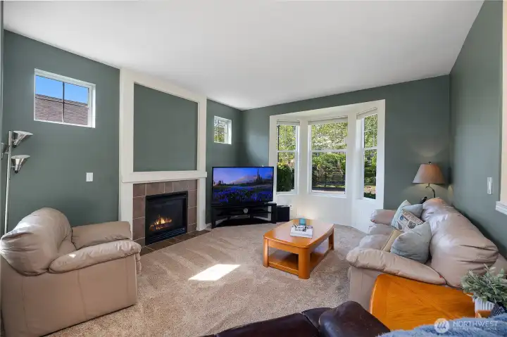 Great room with bright bay windows and gas fireplace leading to dining and kitchen with hardwood floors.