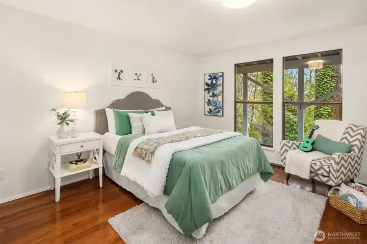 Bright lower-level bedroom featuring hardwood floors and large windows framing tranquil greenery