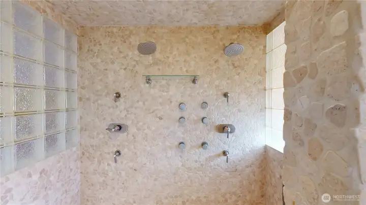 Spa-style custom shower clad in tumbled travertine stone accents and a glass block wall with dual shower heads, one hand-held shower head (not shown) and body sprays.