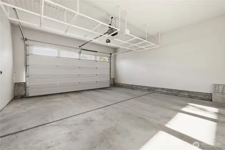 Well-lit garage featuring ample overhead storage, dual EV chargers, and an energy-efficient tankless water heater.