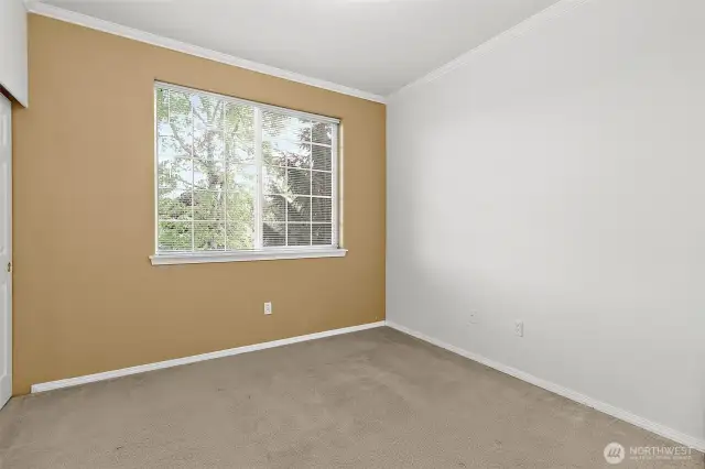 This inviting second bedroom offers a large window that fills the space with natural light and provides a peaceful view of the surrounding greenery. Neutral tones and clean lines create a comfortable and flexible space—perfect for a guest room or nursery.
