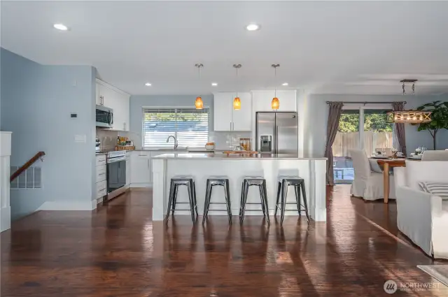 The immaculate, updated kitchen showcases quartz counters, white cabinets, designer lighting, newer stainless steel appliances, and gorgeous engineered hardwood floors.