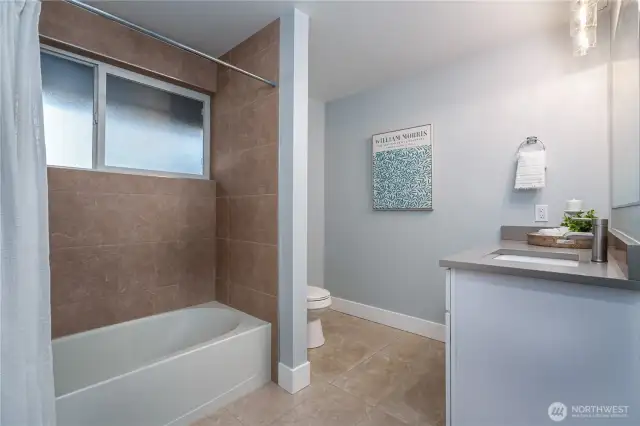 The spacious full hall bath offers quartz countertops, ceramic tile flooring, and a tastefully tiled shower surround.