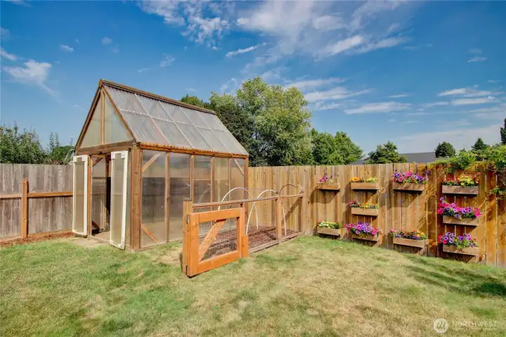 Greenhouse with adjoining fenced garden and flower boxes along the fence.