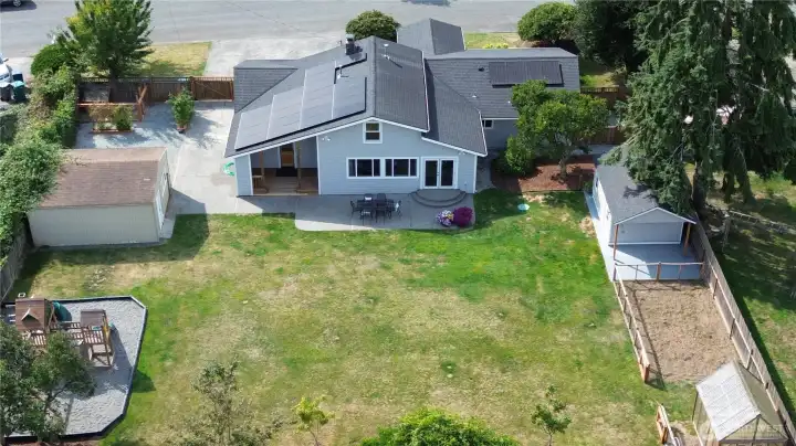 Aerial view of backyard, playground, shed/shop, raised beds, RV parking & dog run on left, newer outbuilding, garden area and greenhouse on right.  Fully fenced backyard.