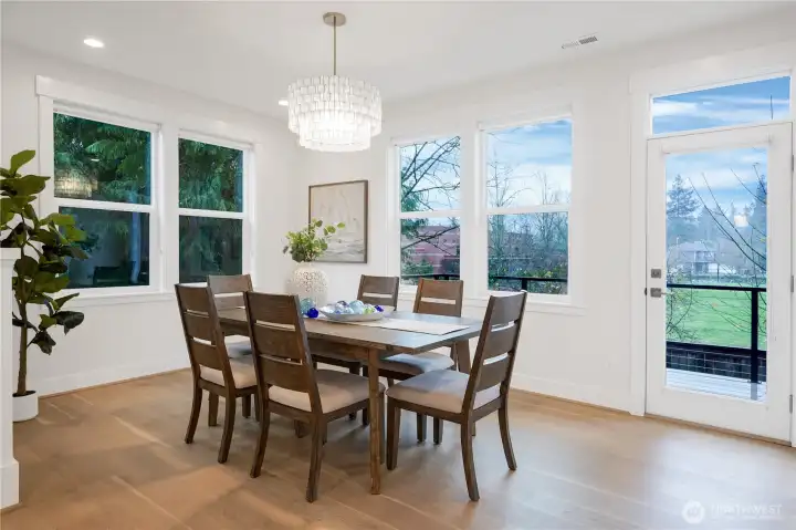 The dining area is bathed in natural light, with serene views over the deck and green field beyond.  A nearby door opens directly to the deck, seamlessly extending your living space and offering the opportunity to enjoy the outdoors.