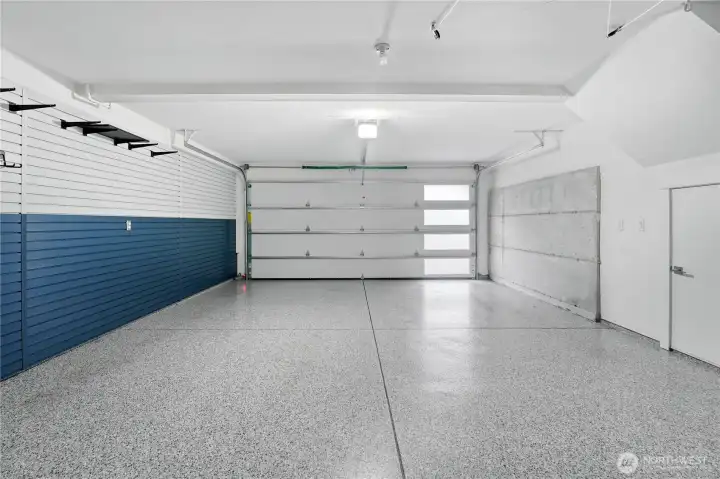 The garage is finished with durable epoxy flooring, offering both style and easy maintenance.  Walls are outfitted top-to-bottom with Slatwall customizable organizers, providing flexible storage solutions for every need.  Just beyond view, a built-in workbench with additional storage completes this highly functional space.