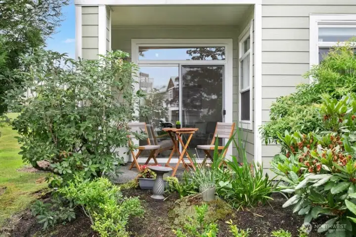 Cozy patio retreat just off the living room, framed by garden greenery with relaxing views and access to the surrounding grassy open space.