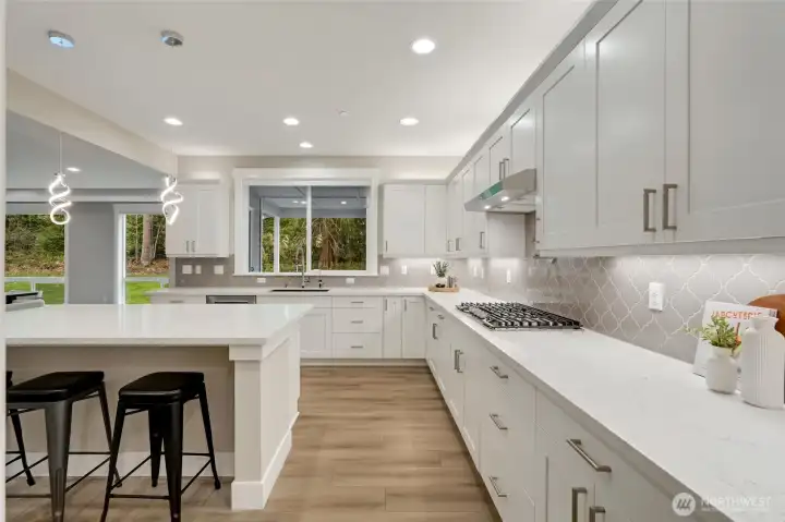 “Expansive kitchen design with a large gathering island, and a window framing private, covered outdoor patio and  fireplace wooded views.”