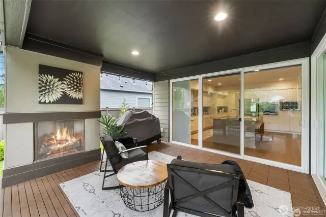 Sliding glass doors open to reveal a covered outdoor terrace with a fireplace and comfortable seating, providing a serene backdrop of the community's natural beauty. Covered for your comfort....