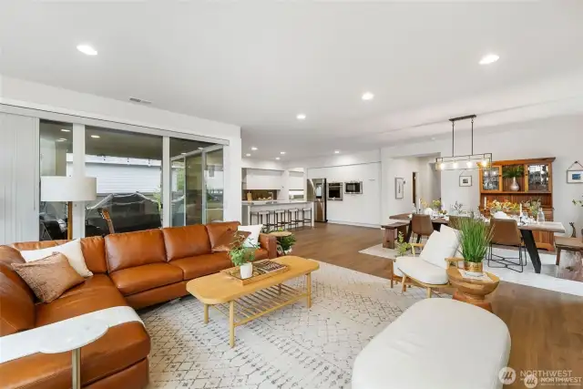The living room portion of this beautiful open concept area has large windows behind the couch showing the covered patio. At the top of the picture is the elegant chef's kitchen with four stools at the dining bar. To the right is the formal dining area.