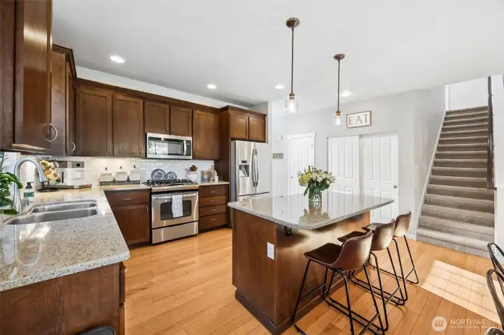 Open kitchen concept with granite countertops, pendant lighting, stainless steel appliances (gas stove), breakfast bar, undermount stainless steel sink & full tile backsplash.