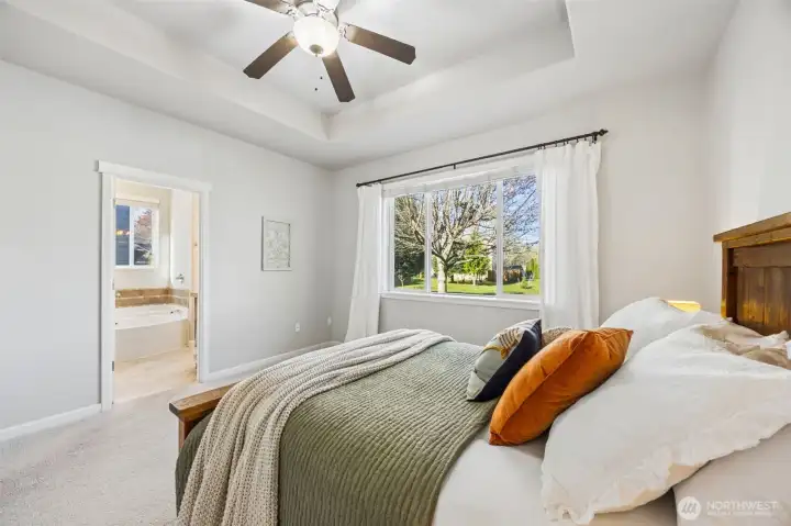 Main floor primary suite with large picture window, ceiling fan, coffered ceiling & double doors leading to the primary bath.