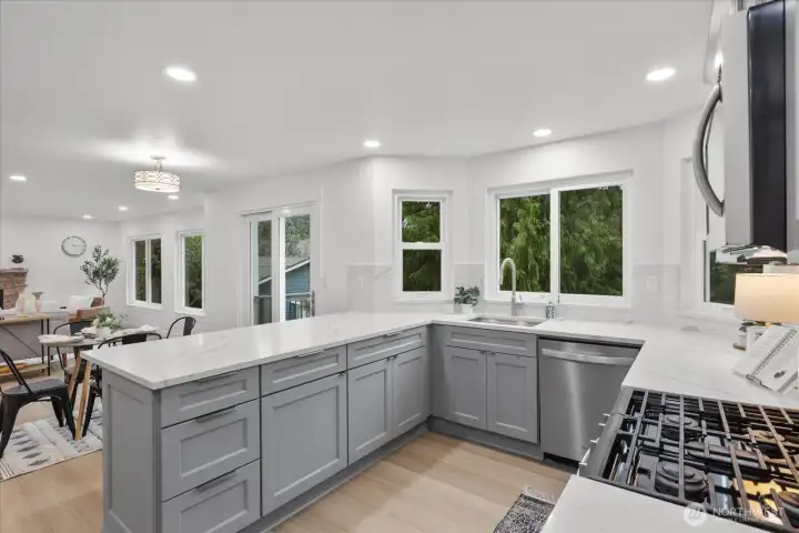Fully renovated kitchen with quartz counters, full-height backsplash, premium shaker cabinets, pantry, deep drawers, and updated stainless steel appliances. Kitchen opens to second dining and living areas.