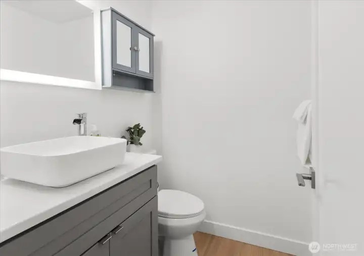 Fully renovated half bath, featuring new grey shaker vanity, luxury vinyl plank flooring, new toilet & Lux Hardwired LED Mirrors.