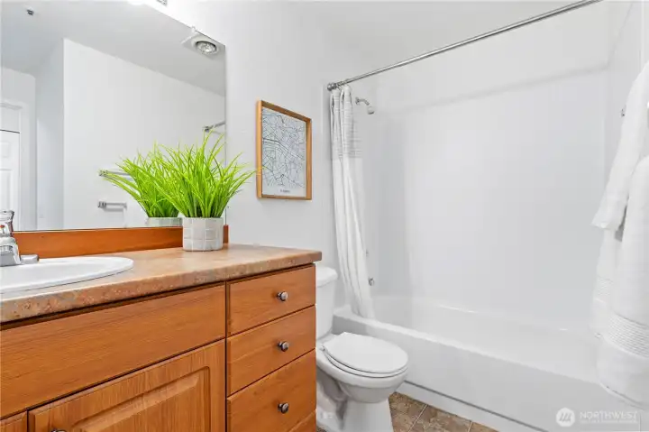 Full guest bathroom down the hallway with fresh interior paint, warm cabinetry and vinyl flooring.