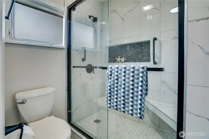 Start your day in style—this updated bath offers a walk-in shower with bench seating, fresh tile, glass doors, and thoughtful finishes throughout.