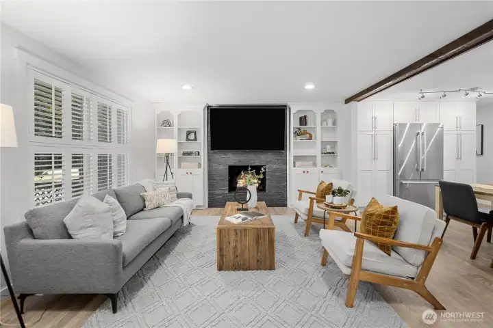 The living room feels bright, calm, and beautifully gathered around the fireplace, where the dark stacked-stone tile adds texture, depth, and a handsome modern contrast against the soft white built-ins. Shelves with classic arched detailing flank each side, bringing symmetry, charm, and graceful display space. The mounted TV stays with the home for an easy, move-in-ready focal point.