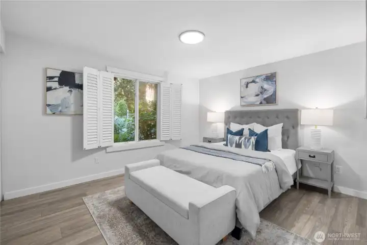 The primary bedroom is spacious enough for a king-size bed, with a large window and classic shutters bringing in natural light and garden views. A modern flush-mount ceiling light casts an even tone throughout the room.