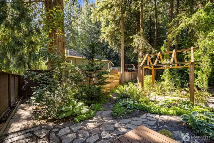 From the deck, stone pathways lead into a beautifully planned backyard, with purposeful plantings layered throughout the garden. Each turn reveals another quiet place to enjoy the greenery, dappled light, and peaceful outdoor setting.