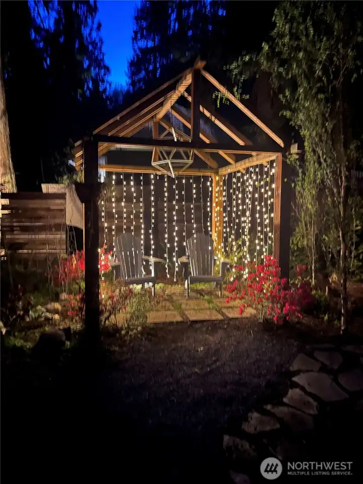 At night, the pergola comes to life in a dreamlike glow, with cascading lights and a sculptural geometric globe overhead that invites the imagination. Imagine warm summer gatherings here with friends and family, or quiet evenings surrounded by the soft sparkle of the garden.