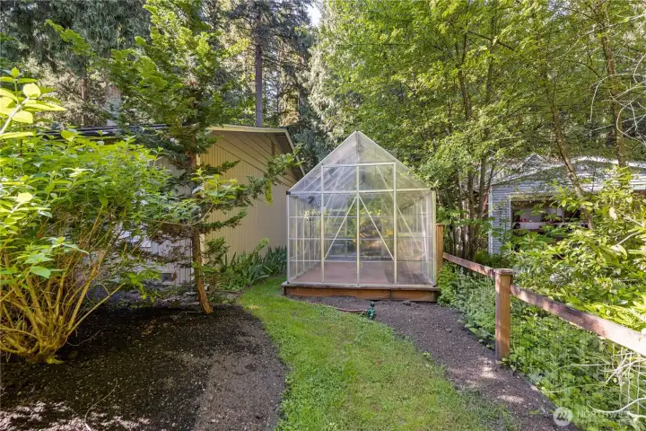 Along the side yard, a greenhouse creates a dedicated place to grow fresh vegetables, herbs, starts, or seasonal flowers. Surrounded by greenery, it gives gardeners a practical spot to enjoy growing through more of the year.