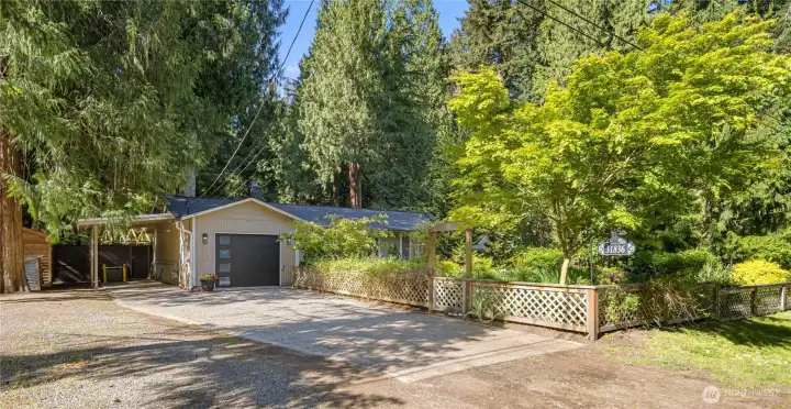 Practical outdoor features are thoughtfully placed here, including an 8x10 shed for garden storage and a small open firewood shed beside the carport. A Honeywell natural gas generator sits at the back of the carport for peace of mind, while a hose bib makes car washing easy. The wooden gate beyond the carport leads to the private backyard, and the driveway plus gravel parking area provide room for multiple cars.