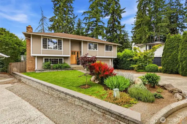 A wide street-level view showcasing the beautifully manicured front yard, raised garden beds, and classic split-level architecture. A wide street-level view showcasing the beautifully manicured front yard, raised garden beds, and classic split-level architecture.