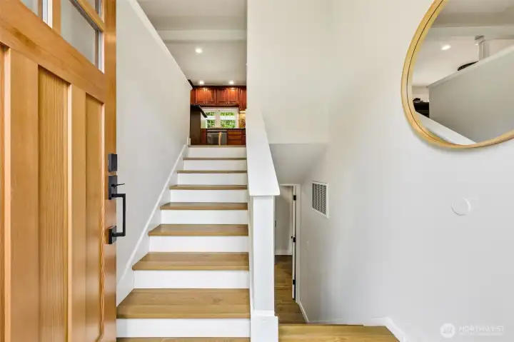 A bright and open foyer with newly finished hardwood stairs, clean white walls, and a glimpse into the kitchen above. A bright and open foyer with newly finished hardwood stairs, clean white walls, and a glimpse into the kitchen above.
