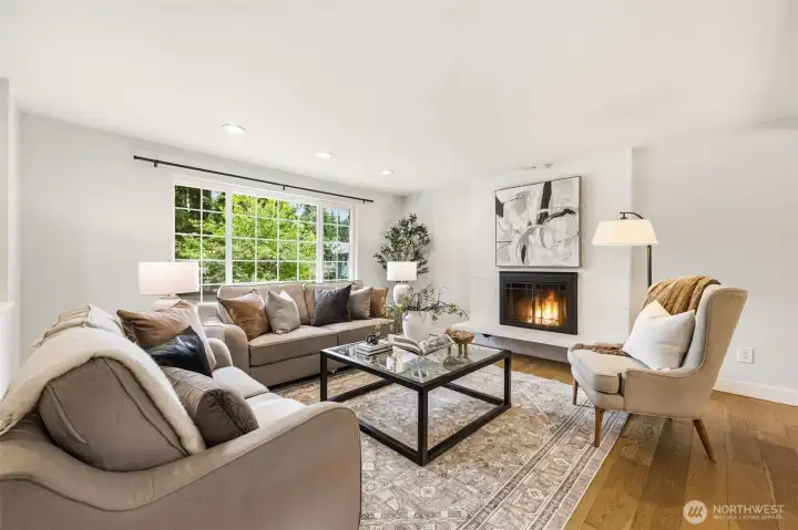 The sun-filled living room offers hardwood floors, a cozy wood-burning fireplace with painted brick surround, and views of the lush backyard. The sun-filled living room offers hardwood floors, a cozy wood-burning fireplace with painted brick surround, and views of the lush backyard.