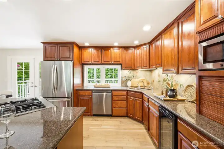 The chef's kitchen features rich wood cabinetry, granite countertops, stainless steel appliances, a wine fridge, and a garden window overlooking the backyard. The chef's kitchen features rich wood cabinetry, granite countertops, stainless steel appliances, a wine fridge, and a garden window overlooking the backyard.