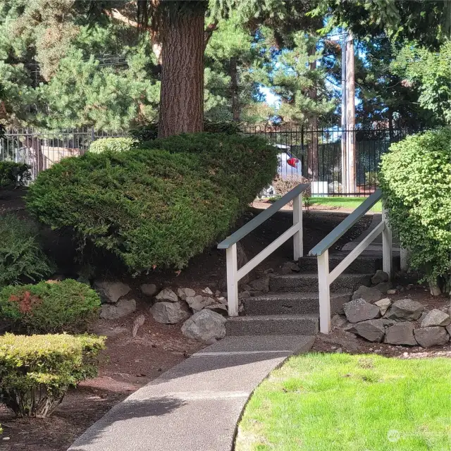 Stairs heading toward front of complex by pool area. Attractive iron fencing. Wooded area across the street from complex adding to a more serene and peaceful setting.