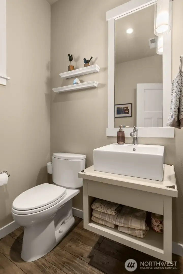 A stylish powder room for guests features custom open shelving cabinetry, an extended mirror, and an opening window that brings natural light in
