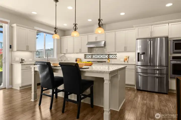 Well-appointed kitchen with oversized island, an abundance of cabinets, gas cooktop, stacked oven and microwave and window over sink